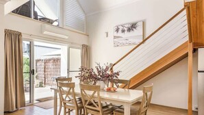 Un comedor con una mesa y sillas, un jarrón con flores, un cuadro en la pared y una escalera.