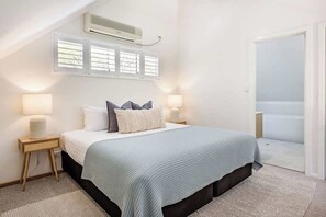 A bedroom with a bed, bedside lamps, a window with blinds, an air conditioner, and a door leading to a balcony. - Villa 1 - Whitesands (Quindalup)