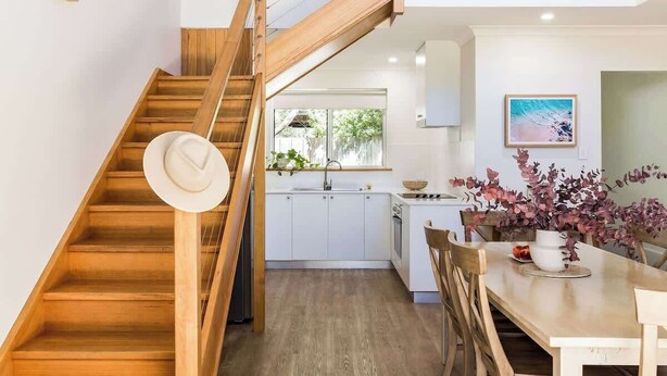 Una cocina moderna con armarios blancos, una escalera de madera y un comedor con una mesa y sillas.