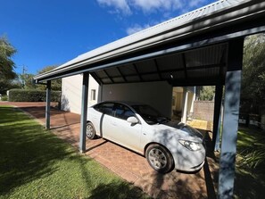 A white car parked under a covered area with a brick pathway leading to a building.