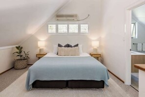 A bedroom with a bed, bedside lamps, a potted plant, and a window.