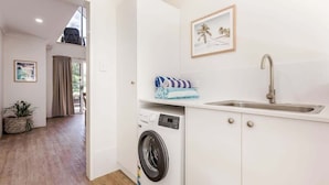 Una cocina compacta con lavadora, un lavamanos y una ventana con cortinas.
