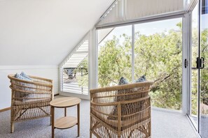 A room with two wicker chairs and a small table, large glass doors leading to an outdoor area with trees.