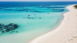 Una playa costera con aguas turquesas cristalinas, barcos y una orilla arenosa.