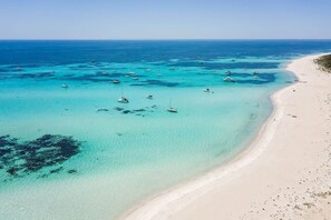 A coastal beach with clear turquoise waters, boats, and a sandy shore.