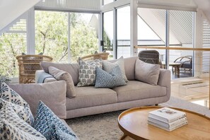 A modern living room with a sofa, patterned cushions, a wicker chair, and a coffee table with books. - Villa 1 - Whitesands (Quindalup)