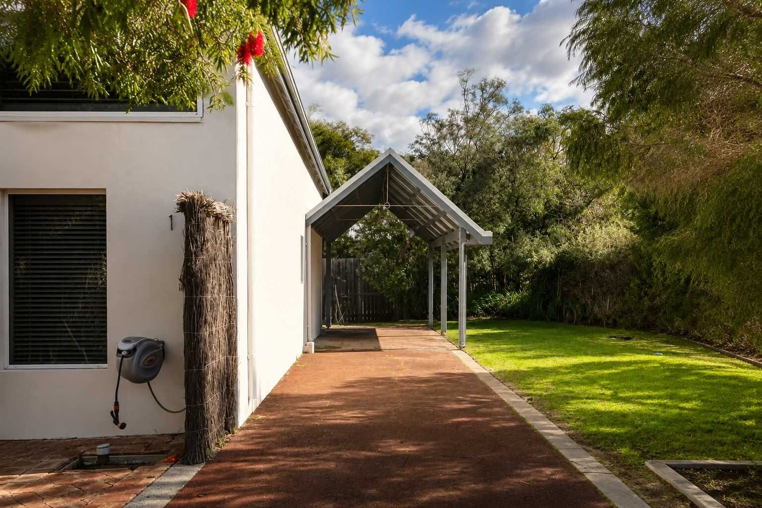 A covered outdoor area with a pathway leading to a building, surrounded by lush greenery.
