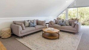 Un dormitorio tipo loft moderno con un ventanal grande, dos sofás, una mesa de centro redonda y una alfombra estampada.