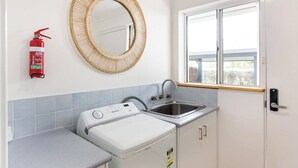 Cozinha compacta com máquina de lavar, pia, extintor de incêndio e janela com vista.
