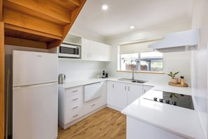 A modern kitchen with white cabinetry, a microwave, a sink, and a stove.