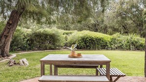 Uma mesa de piquenique de madeira com um banco, rodeada por um espaço gramado e vegetação densa.