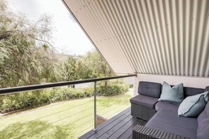 Un balcon avec un canapé gris, une rambarde en métal et une vue sur un espace verdoyant avec des arbres.