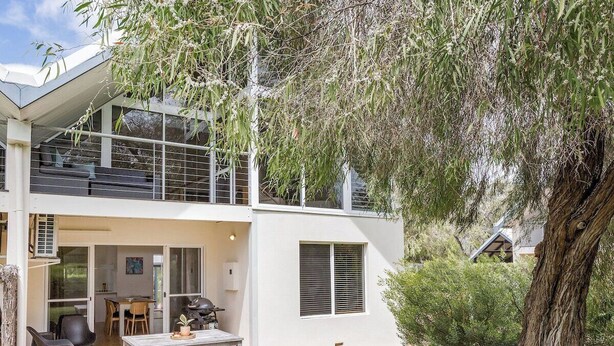 A two-story house with a patio, outdoor seating, and a large tree. - Whitesands Villa 3 (Quindalup)