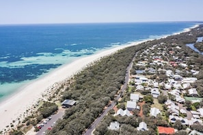 Vue aérienne d’une zone résidentielle côtière, avec des maisons, une plage et une eau d’un bleu limpide.