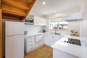 A modern kitchen with white cabinetry, a microwave, a sink, and a stove.