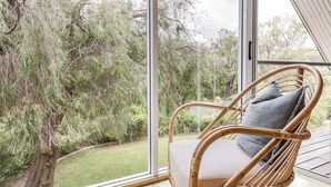 Uma cadeira de vime com almofada em um quarto com grandes janelas dando para um jardim.