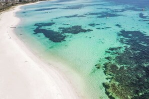 Une plage aux eaux turquoise et limpides, un rivage sablonneux et des bateaux ancrés à proximité.