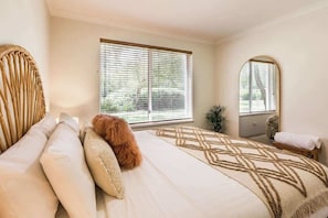 Ein Schlafzimmer mit Bett, einem Fenster mit Jalousien, einem Spiegel und einer Topfpflanze.