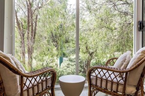A room with wicker chairs and a round table, a large window with a view of trees.