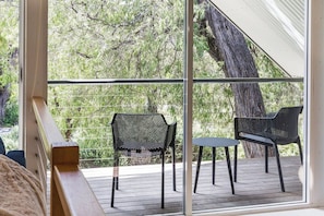 A balcony with two chairs and a table, overlooking a wooded area.