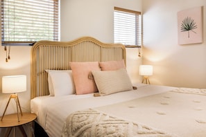 A bed with a wooden headboard, two bedside lamps, and a wall-mounted plant.