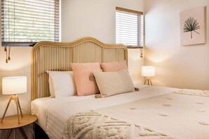 A bed with a wooden headboard, two bedside lamps, and a wall-mounted plant.