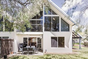 A modern two-story house with a patio, a covered outdoor seating area, and a large window.