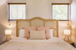 A bed with a headboard, two bedside lamps, and a window with blinds.