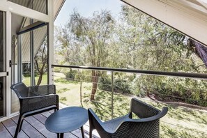 A balcony with two chairs and a table, overlooking a garden with trees and a fence.