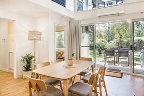 A spacious dining area with a wooden table and chairs, a potted plant, and a view of the outdoors through large sliding doors.