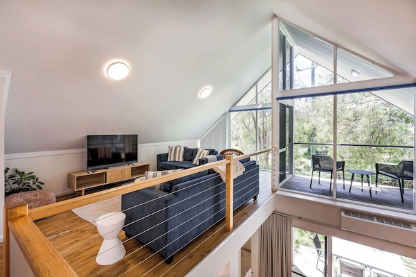 A modern living room with a large window, a sofa, a television, and a wooden staircase.