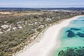 Eine Küstenlandschaft mit Sandstrand, dichter Vegetation und vereinzelten Gebäuden.