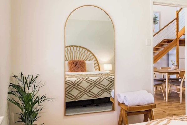 A hotel room with a bed, a mirror, a plant, a wooden bench, and a staircase.