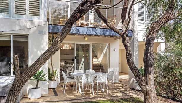 Un espacio al aire libre moderno con una mesa y sillas, rodeado de plantas en macetas y árboles.