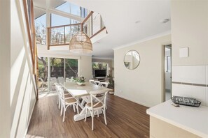 A modern dining area with a large table, white chairs, and a hanging light fixture.
