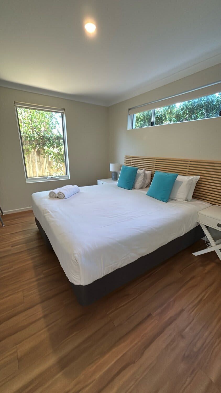 Une chambre moderne avec un grand lit, une table de chevet, une commode et une fenêtre donnant sur un paysage verdoyant.