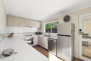 Une cuisine moderne avec des meubles blancs, des appareils en acier inoxydable, un four à micro-ondes et une horloge au mur.