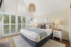 A bedroom with a large bed, bedside tables, a hanging light fixture, and a window with blinds.