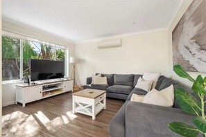 A living room with a TV, sofa, coffee table, and a plant.