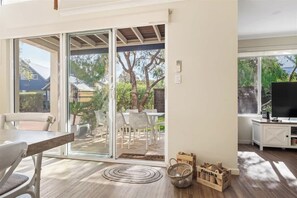 A room with a sliding glass door leading to an outdoor patio, a dining table with chairs, a television, and a white cabinet.