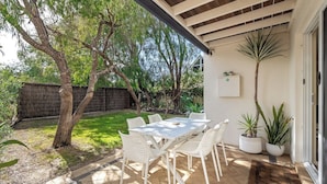 Un patio al aire libre con mesa y sillas, rodeado de plantas y árboles.