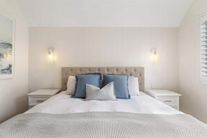 A bedroom with a tufted headboard, two bedside tables, a bed with a patterned bedspread, and two wall-mounted lights.