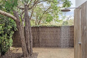 A tree, a wooden wall, and a showerhead in a courtyard.