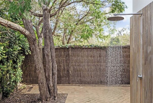 Un arbre, un mur en bois et une pomme de douche dans une cour.