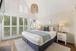 Une chambre avec un grand lit, une table de chevet avec des lampes et une fenêtre avec des stores.