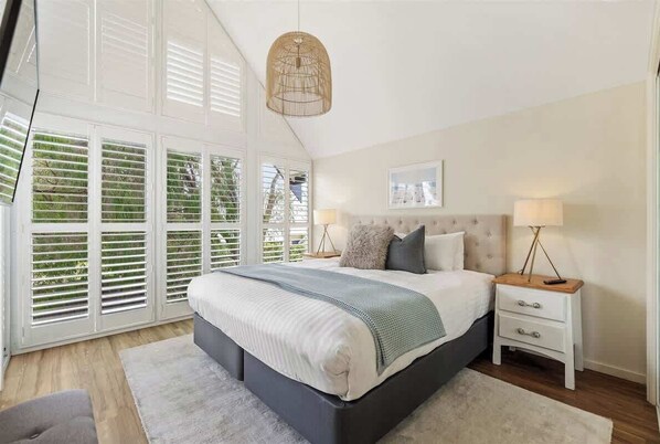 A bedroom with a large bed, a bedside table with lamps, and a window with blinds.