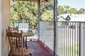 A balcony with a table and chairs, a view of parked cars, and a building with a green roof in the background. - Lana Studio—Central Base for South West Adventures (Margaret River)