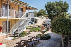 A building with a balcony, a staircase, and a garden area with a fountain and picnic tables.