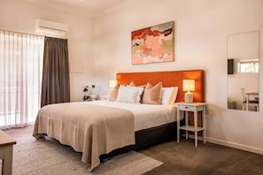 A hotel room with a bed, bedside tables, a mirror, and a painting on the wall.