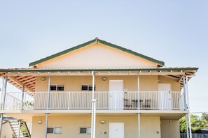 Un edificio a due piani con un balcone al piano superiore, una porta al piano inferiore e una piccola finestra al piano superiore.